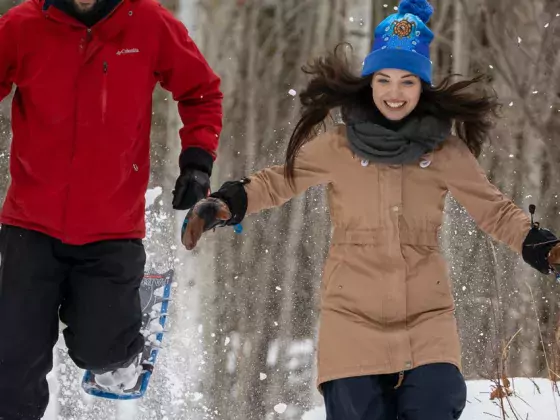 Two People running down a trail in snowshoes.